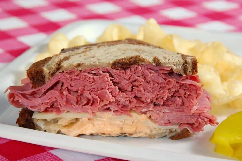 A Reuben sandwich served with chips and pickles